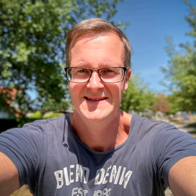 Selfie einer Person mit kurzen Haaren und Brille, draussen in der Sonne